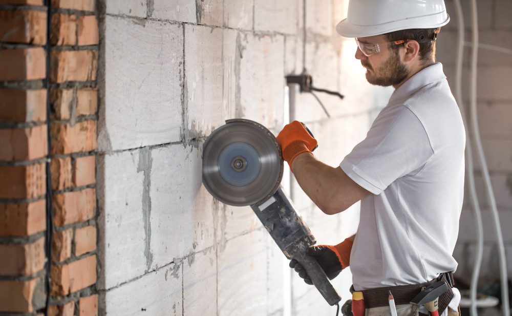 The industrial Builder works with a professional angle grinder to cut bricks and build interior walls. Electrician. The industrial Builder works with a professional angle grinder to cut bricks and build interior walls. Electrician.